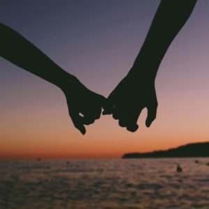 Silhouetted hands holding at sunset over a calm ocean. Romantic and peaceful seascape.