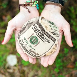 Hands holding crumpled money outdoors, symbolizing charity and financial support.