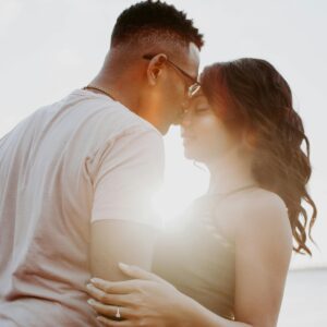 A couple embraces on a beach at sunset, capturing a moment of romance and affection.