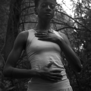 Black and white photo of a woman meditating in a serene forest, eyes closed.