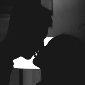 Silhouette of a couple kissing in a romantic and intimate moment against a bright light.