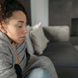 Young woman resting at home, wrapped in a blanket and feeling unwell, conveying a sense of illness or discomfort.