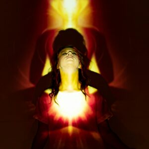 A woman meditates with a vibrant aura and light projections creating a spiritual ambience.