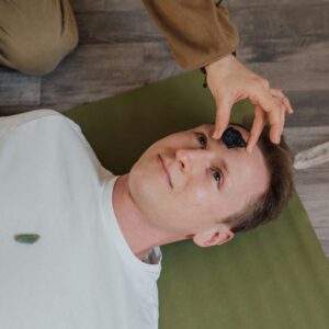 A man lying down during a crystal healing ritual indoors on a yoga mat.